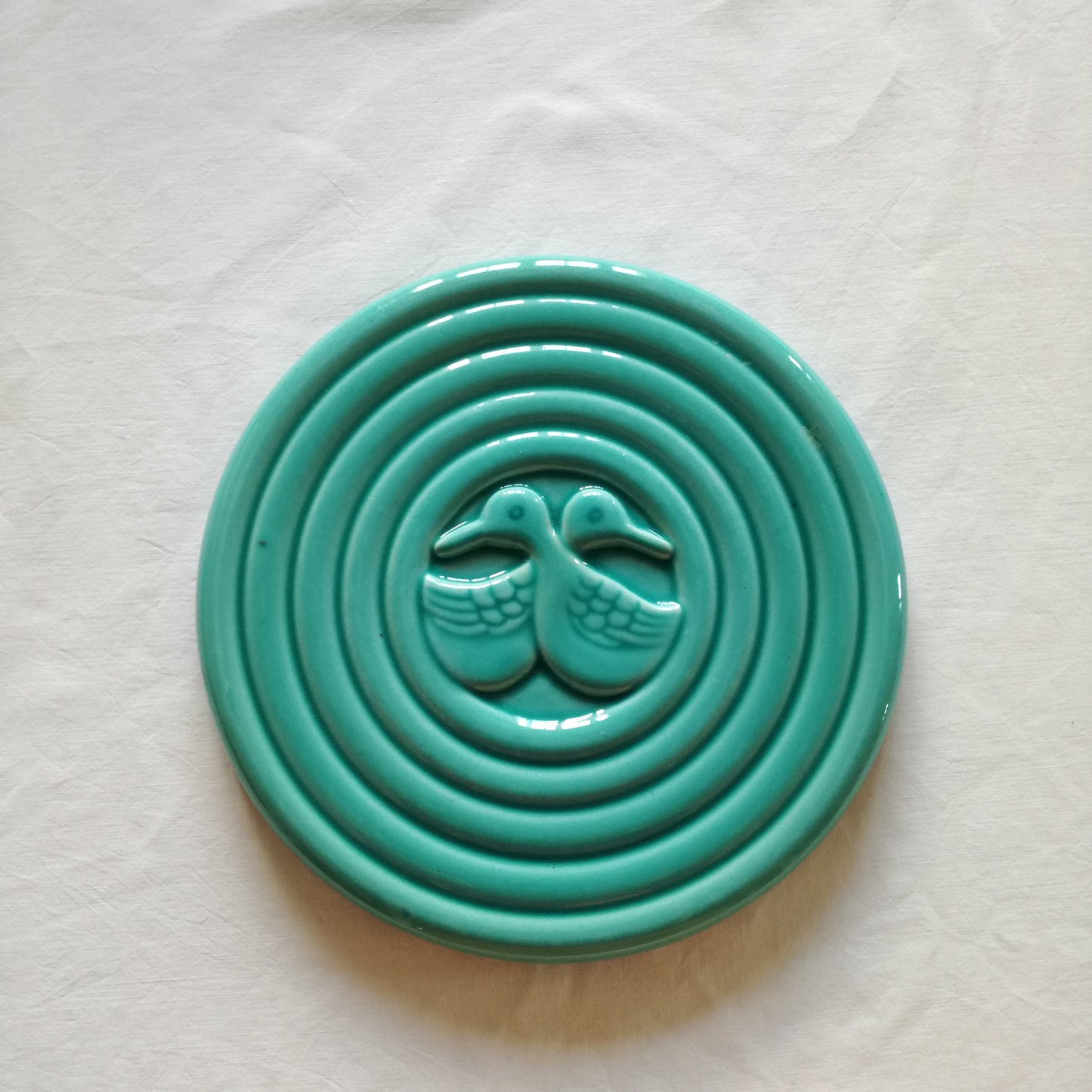 Dessous de plat en céramique vert clair à décor central de canards enlacés